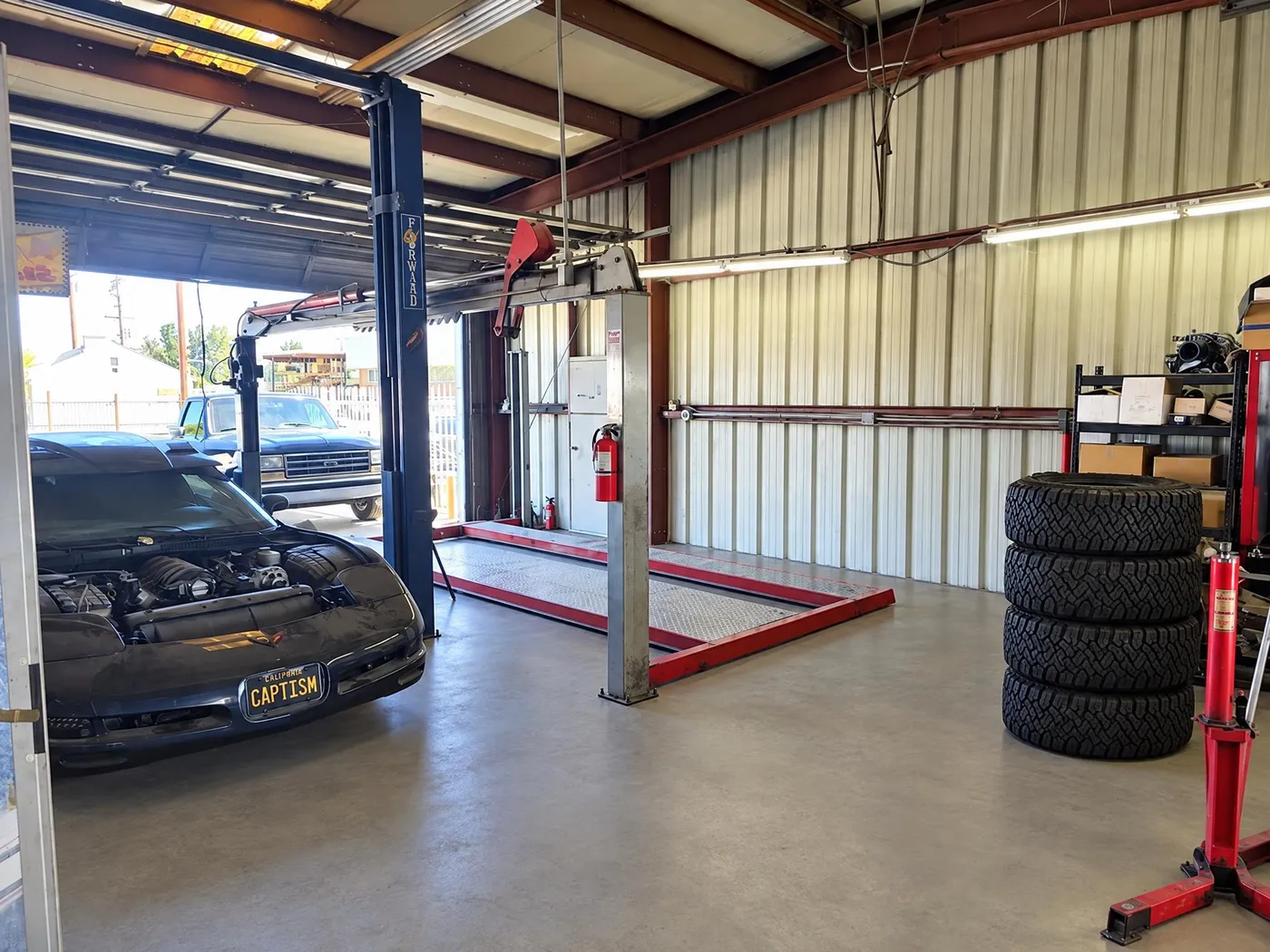 Service bay with a black Corvette, engine crane and four-post lift